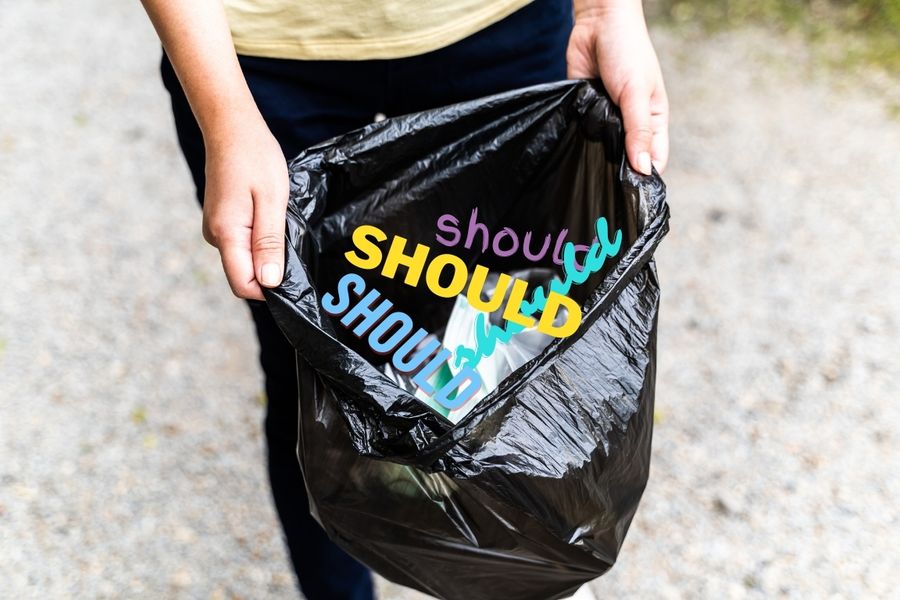 woman holding garbage bag full of "shoulds"