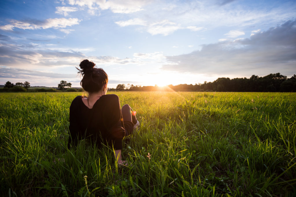 woman in green field looking at sunset