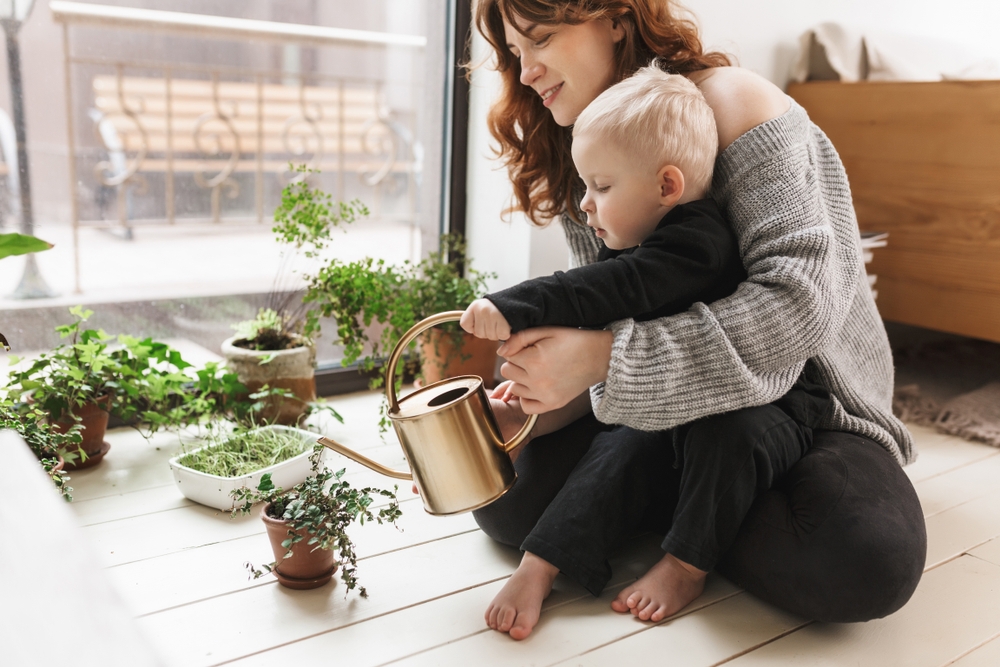 Mom in black stretchy pants watering flowers with baby