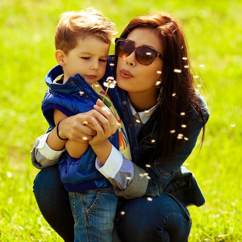 Mom in jean jacket blowing dandelion with little boy