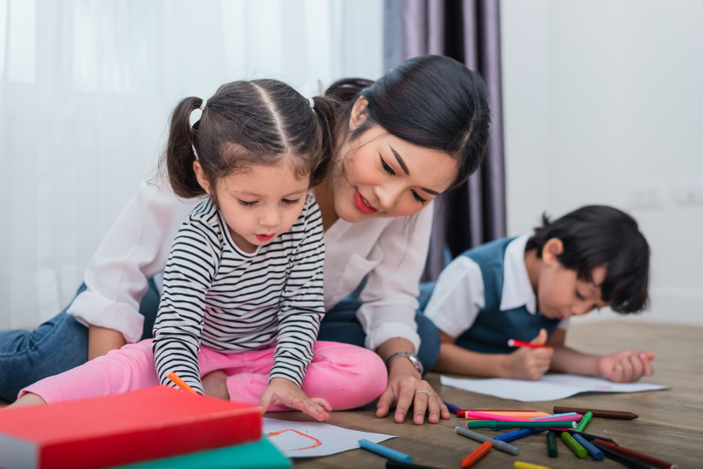 Mother with hair in pony tail working with kids doing homework on the floor