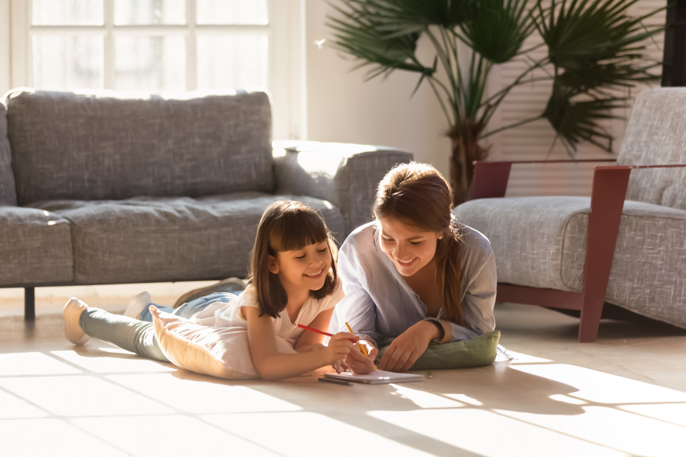 Stylish Mom with hair pulled back helps daughter with homework on floor