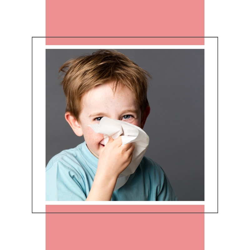 little boy smiling with tissue held to nose