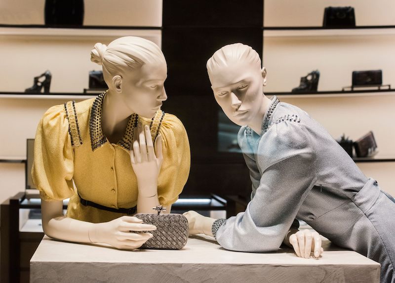 two mannequins leaning over luxury store counter as if talking to one another