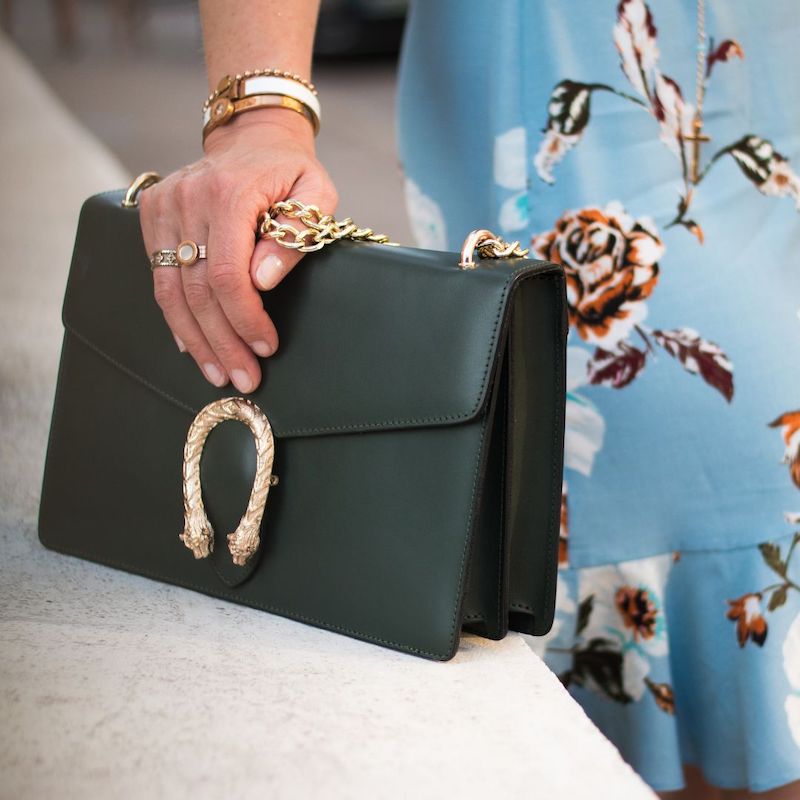 woman in turquoise skirt holding dark green handbag with gold leopard detail