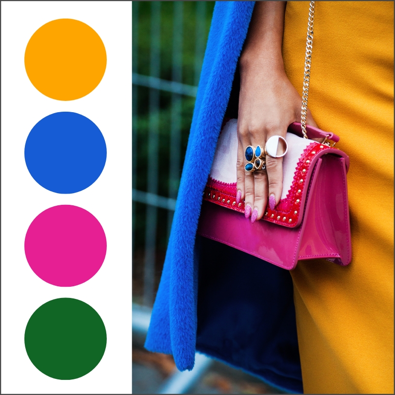 woman wearing yellow orange dress with bright blue coat and dark pink handbag