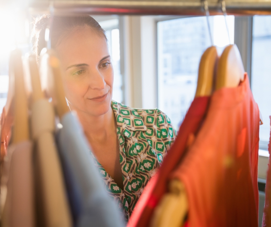 woman wearing green patterned shirt looking at colorful hanging shirts