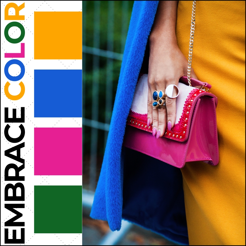 woman wearing yellow orange dress with bright blue coat and dark pink handbag next to colorful dots