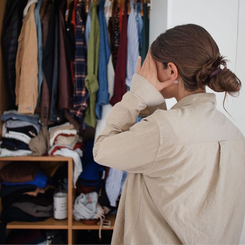 overwhelmed woman in front of messy, disorganized closet holds hand to forehead