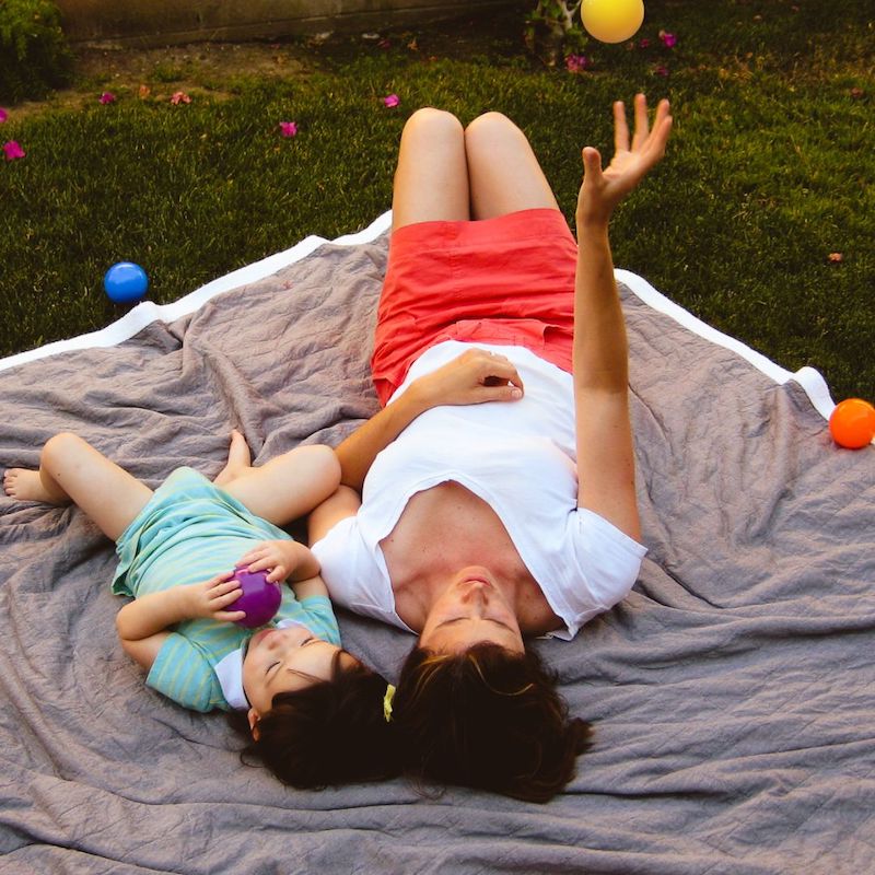 Erin Ross and her toddler daughter laying on a blanket throwing balls in the air